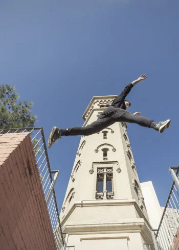 Person parkour jumping between buildings under clear blue sky.