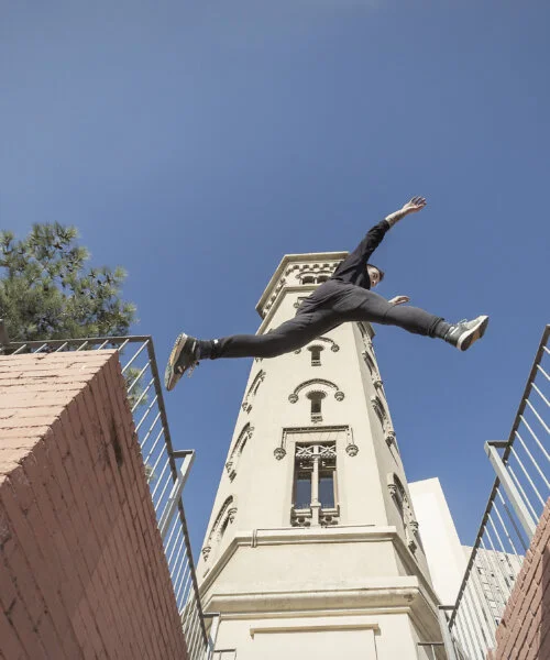 Person parkour jumping between buildings under clear blue sky.